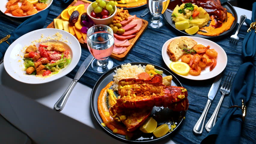 Variety of dishes on a restaurant dinner table. Top view of multiple plates with salad, shrimp, charcuterie board, salmon, and steak on a blue tablecloth.