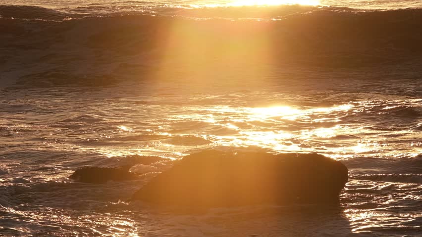 A breaking ocean wave backlit by the sun during sunset. Filmed in Costa da Caparica, Portugal, the visuals highlight nature and the movement of water.