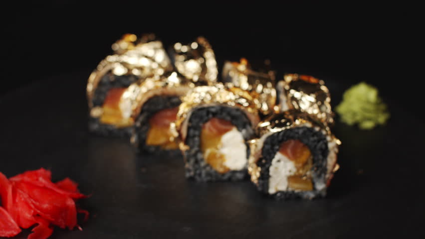 Exclusive golden leaf sushi rolls with black rice, salmon, and cream cheese rotating on a black stone plate, showcasing a luxurious Japanese culinary masterpiece