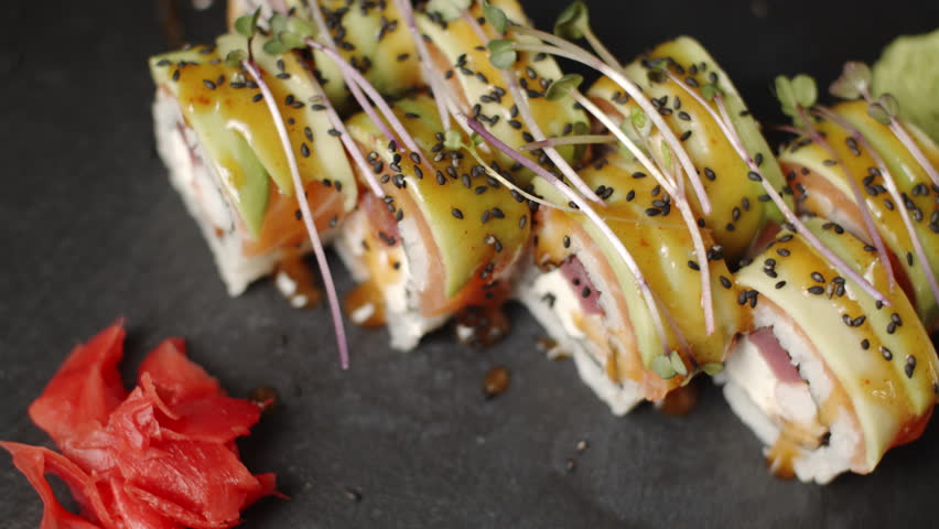 Delicious sushi rolls with avocado, salmon, and tuna served with pickled ginger on a dark slate plate showcasing exquisite Japanese cuisine and culinary presentation