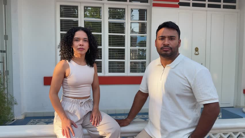 Happy young multiracial couple smiling at the camera and gesturing thumbs up in front of their house