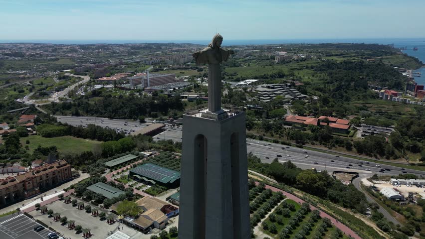 Drone aerial of the monumental Christ King statue overlooking the Tagus River and Lisbon skyline under clear sunny sky