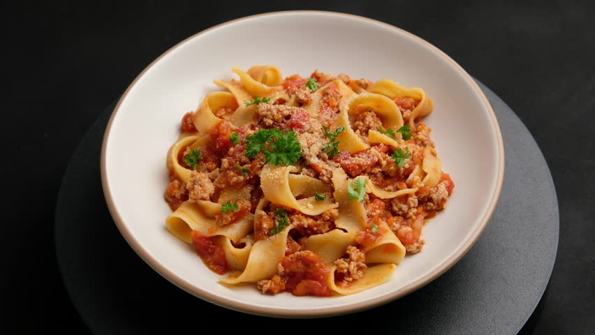 pappardelle pasta with Ground meat and tomato,spaghetti with a meat based bolognese tomatoes,served on white plate with parmesan cheese.