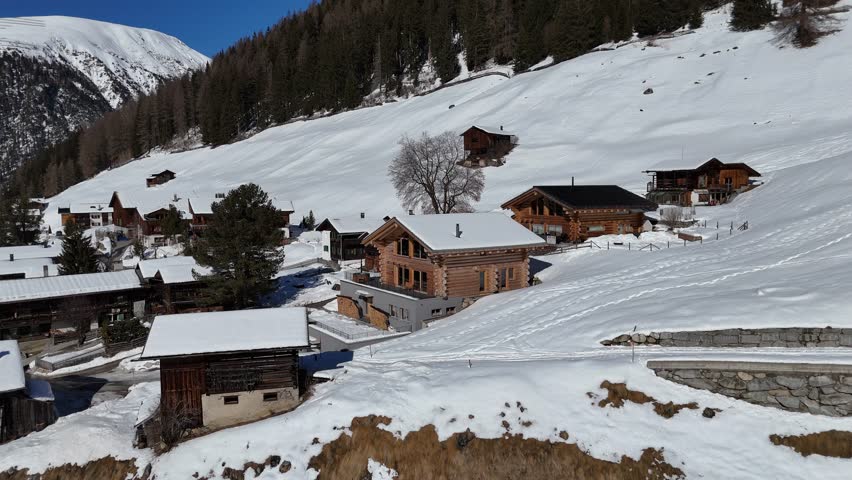 Panning shot revealing a traditional wooden chalet on a snowy mountain slope in a swiss alpine village