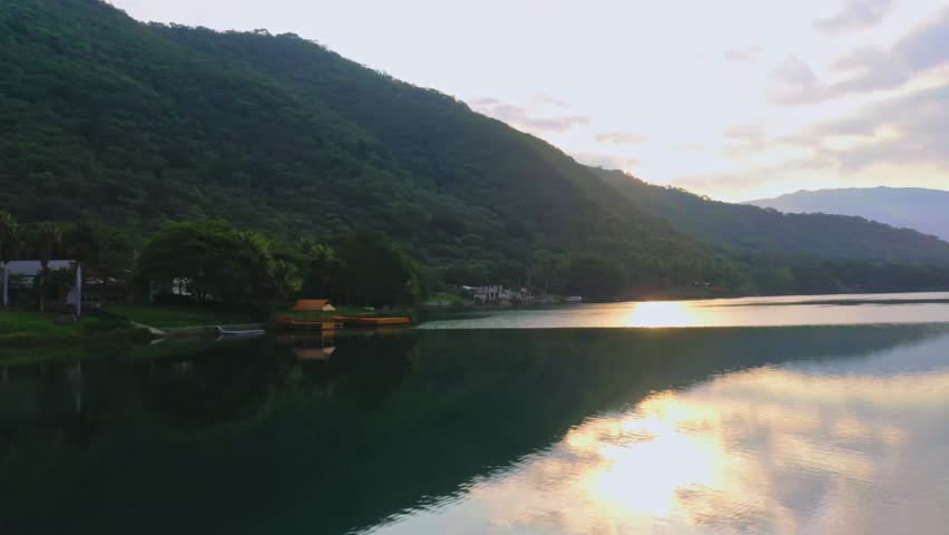 Serene lake at sunset with lush green mountains and golden light reflection