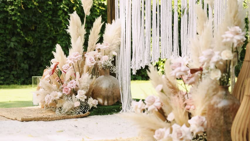 Pastel wedding arch adorned with pampas, blush roses and trailing macrame, sunlit garden setting, layered