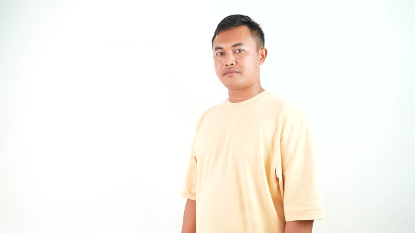 Smiling Asian Man in Yellow Shirt Pointing Forward Isolated on White Background