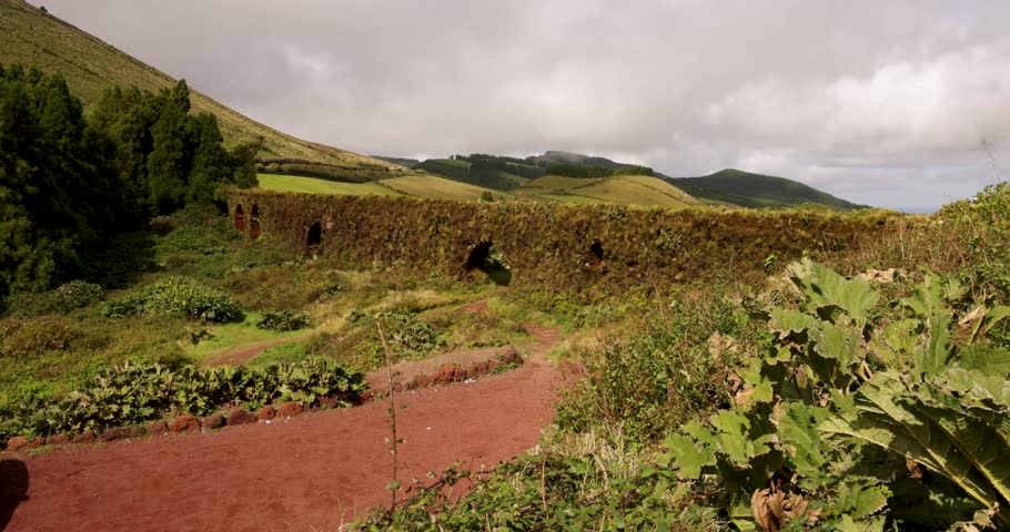 An aqueduct wall and arch with a lush green landscape in the background in Sao Miguel, Azores. The scene is peaceful and serene. Panning shot.
