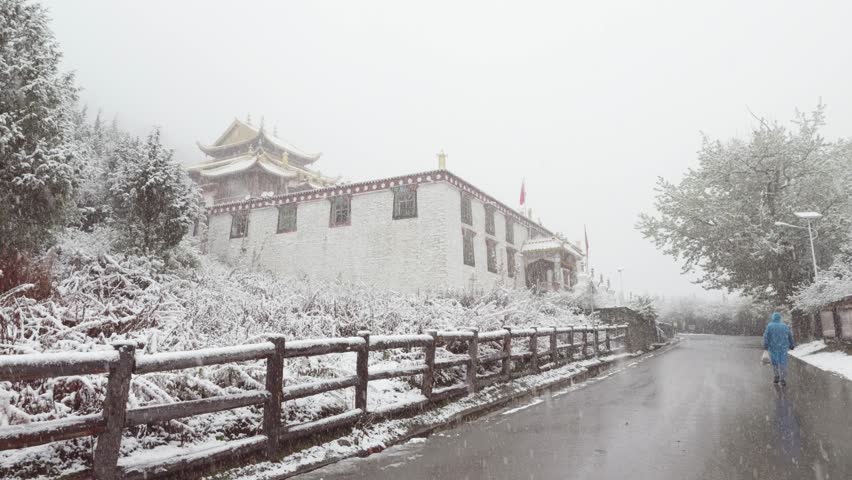 Rear view of unknown tourist or prayer in blue disposable raincoat walking towards lama temple in Changping valley in Siguniang mountains in heavy snowing day, 4k slow motion footage.