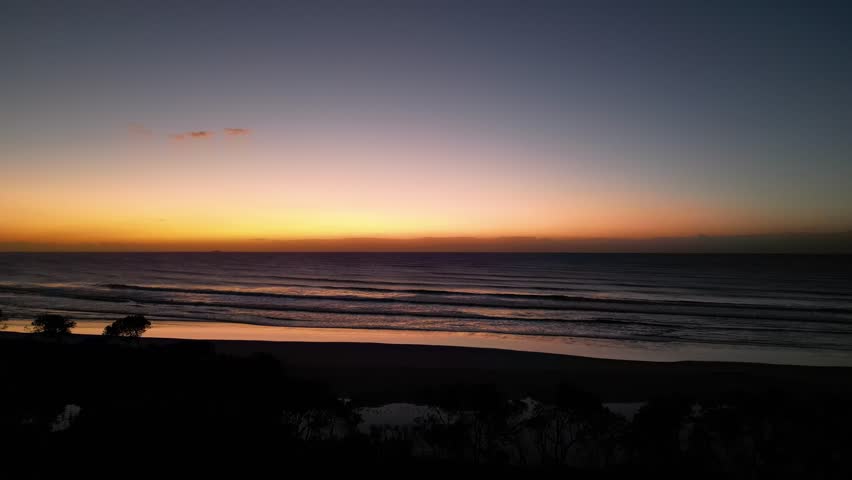 Sunrise over Pacific Ocean waves as camera pans north along Bonny Hills coastline
