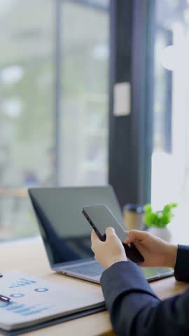 Close-up of Asian businesswoman using mobile phone, texting and cheating on her smartphone while outside office.