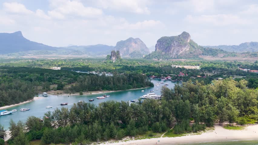 Wide aerial shot of turquoise water, speedboats, and lush mountains under a bright sky