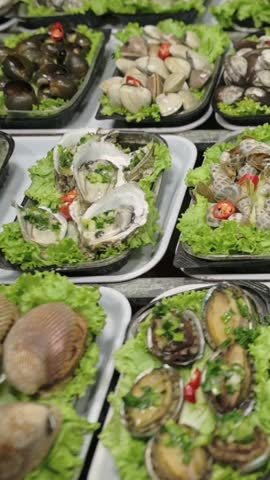 Vertical screen Assorted Oysters, Snails And Mussels On Lettuce Trays, Vendor Presents Steamed And Seasoned Shellfish With Chili And Herbs, Closeup Of Glistening Shells, Lively Street Market