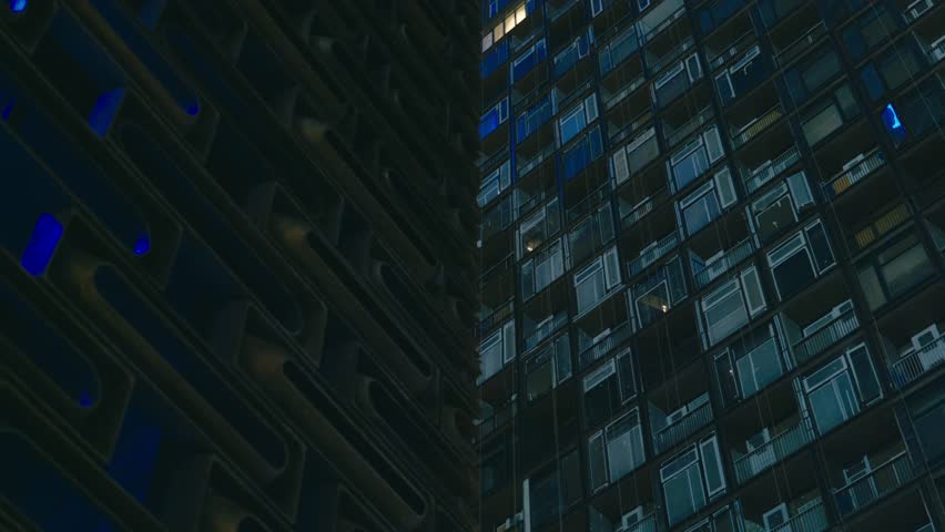 Panoramic view of apartment buildings and skyscrapers in downtown Hong Kong, China at night, illuminated by city lights and glowing windows.