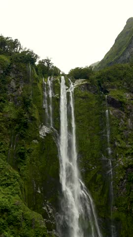 Vertical shot of Stirling Falls in Milford Sound Piopiotahi Fiordland National Park South Island New Zealand water pours down lush cliff into fjord creating misty scenic nature travel background