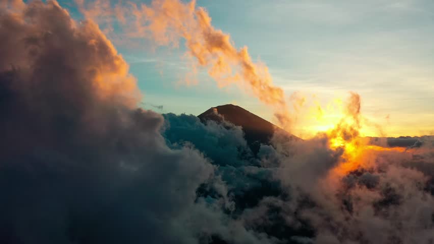 Aerial View Scenery of Large Soft Clouds Moving Gently Around High Mountain Summit. Cloudscape with Morning Sun Painting Sky in Pastel Colors and Gold Tones Creating Dreamy Vibe Outdoors Landscape 4k