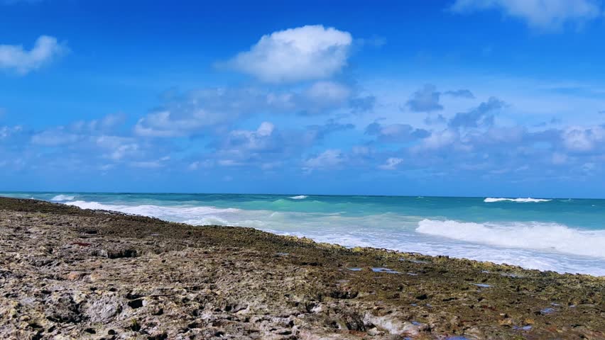 Rocky Cuban beach in Varadero, Cuba, on a cloudy day, when the sun breaks through the clouds, you can see the waves and ocean expanses. Turquoise waves. Stone slabs on the beach in the ocean. 4K	