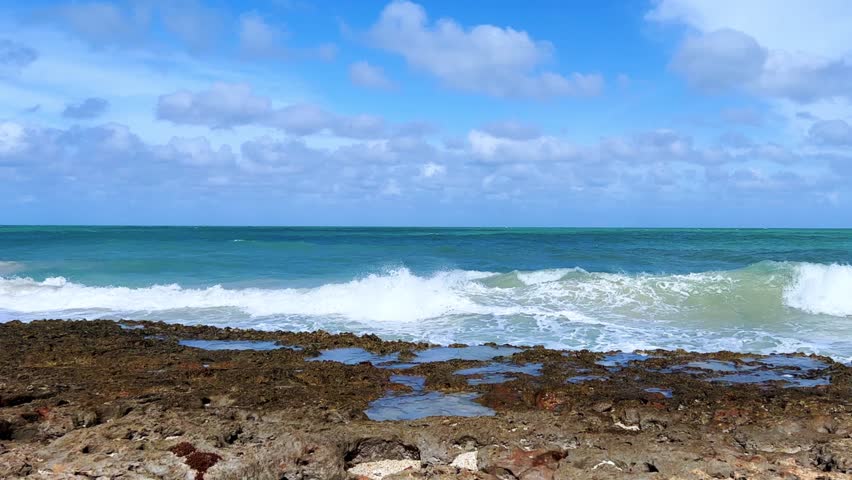 Rocky Cuban beach in Varadero, Cuba, on a cloudy day, when the sun breaks through the clouds, you can see the waves and ocean expanses. Turquoise waves. Stone slabs on the beach in the ocean. 4K	
