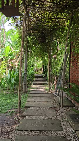 Peaceful stone garden path under a green bamboo trellis and lush tropical foliage in the Mekong Delta, Vietnam.
