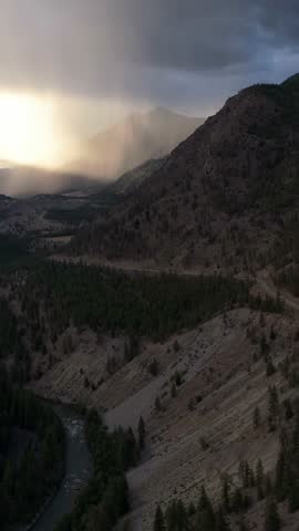 Aerial view captures a breathtaking mountain valley, a winding river, and a road under dramatic sun rays in British Columbia.