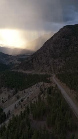 Breathtaking aerial view of a forested valley with a river and winding road under a dramatic, sun-kissed sky in British Columbia, Canada.