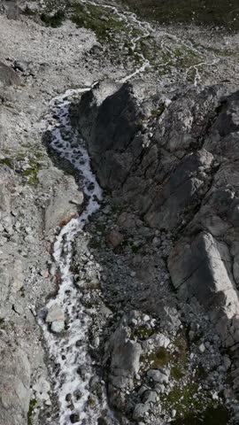 A high-angle drone shot captures a rapid stream winding through a barren, rocky terrain in the stunning landscapes of British Columbia, Canada.