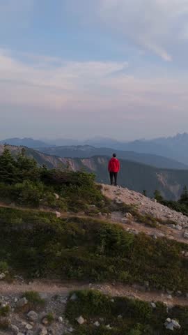 A lone hiker in a red jacket admires the breathtaking mountain landscape of British Columbia, Canada.