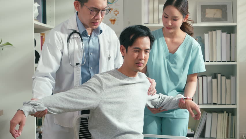 Physical therapist guiding male patient through arm rehabilitation exercise while doctor monitors progress in clinic, healthcare recovery, physiotherapy treatment and medical consultation concept.