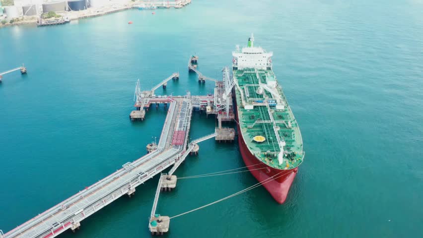 A large cargo ship anchored at an industrial port, showcasing loading and unloading activities against a clear blue sea.