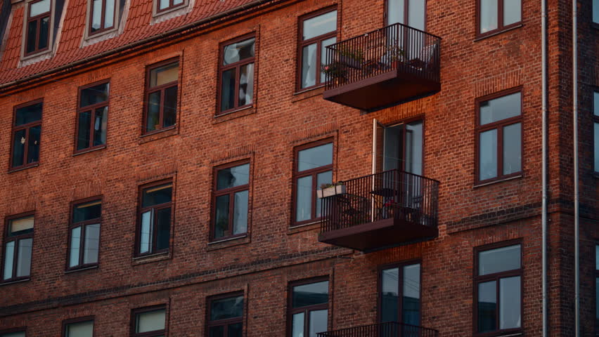 Old brick apartment building facade showcasing windows, balconies, and a tiled roof in an urban setting. Copenhagen, Denmark