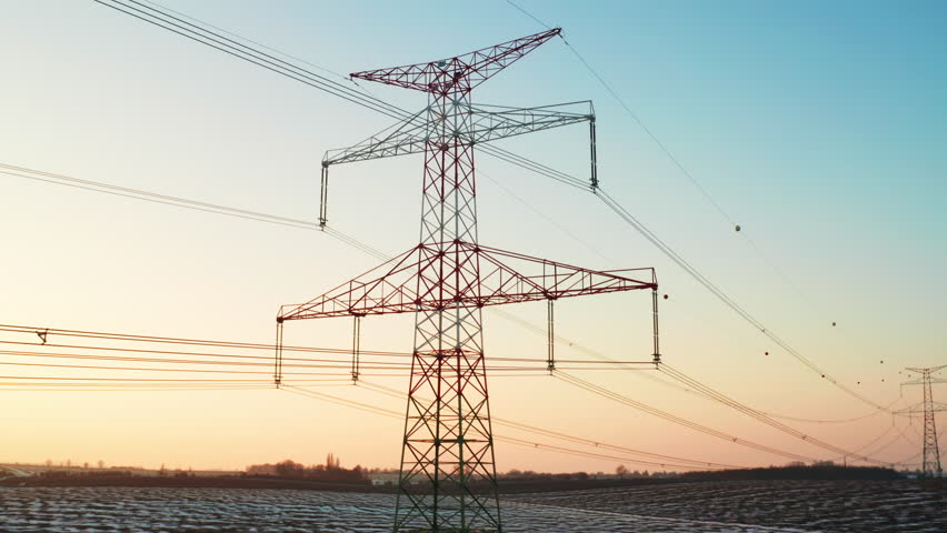 Aerial view of electricity transmission towers in a snowy field during sunset, symbolizing energy infrastructure and green energy distribution.