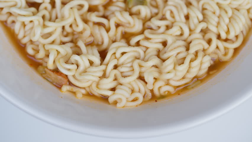 Steaming noodle bowl. Delicious warm instant noodles. Closeup of freshly cooked curly noodles in broth. White bowl filled with steaming flexible noodles in light broth