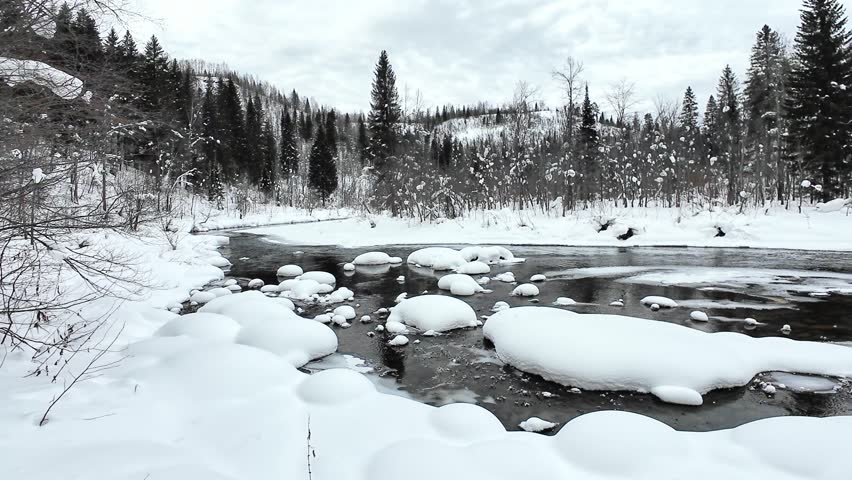 Calm Winter Stream With Trees. Silent Icy River Flowing Past Forested Banks. Peaceful Winter Landscape With Flowing Dark Water And Rounded Ice Formations Along Wooded Riverbanks