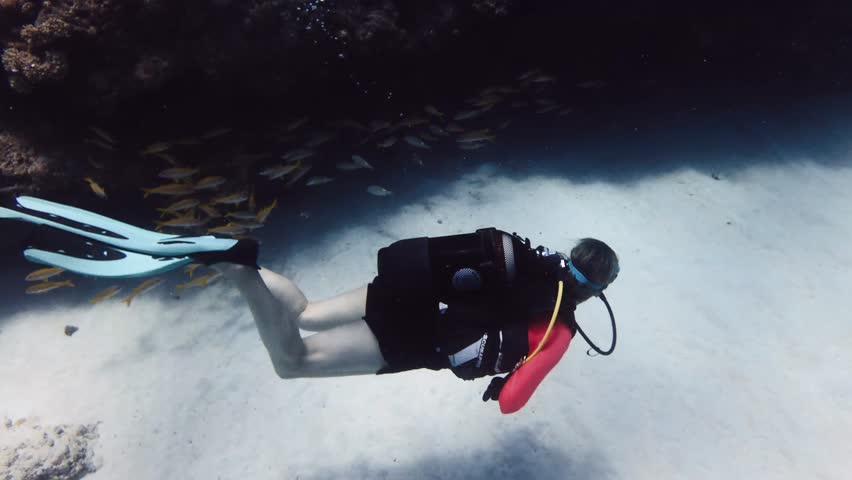 Two scuba divers slowly explore the sandy seabed along a reef wall in the clear waters of Mauritius. Peaceful underwater travel scene ideal for diving tourism, marine exploration, and ocean adventure