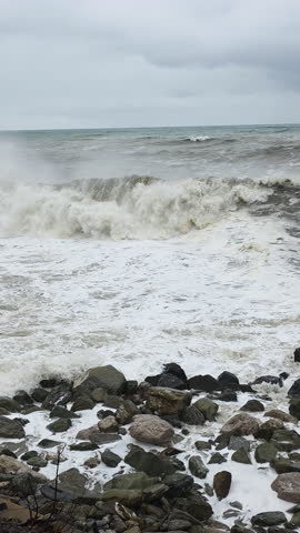 Stormy ocean scene. Fierce surf colliding with jagged coast beneath gray skies. Photographer captures tumultuous ocean pounding rocky coast under gloomy overcast weather conditions