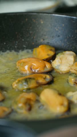 Delicious shelled mussels cooking in hot frying pan with simmering melted butter, creating an aromatic and appetizing gourmet seafood dish perfect for restaurant or home kitchen preparation. Vertical