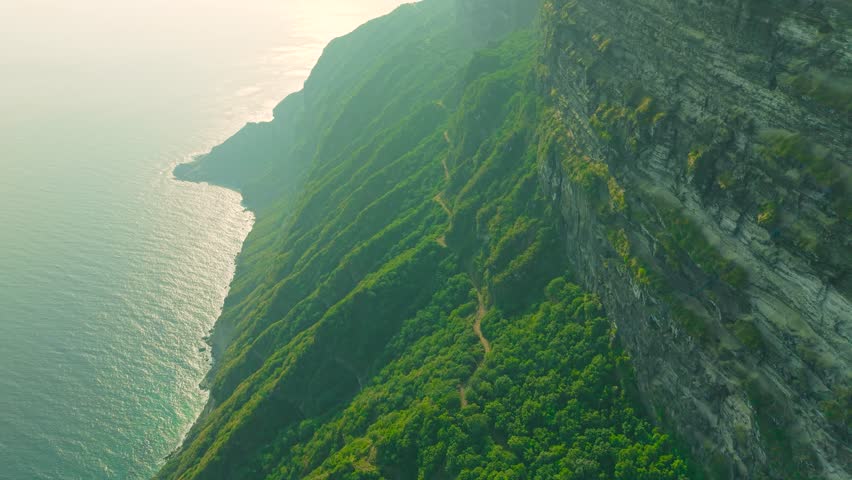 Aerial view of steep green cliffs and a narrow dirt road along the coast at Jabal Shaat on the border between Oman and Yemen.