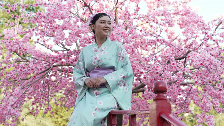 cheerful woman in yukata (kimono dress) with sakura flower or cherry blossom blooming in the garden