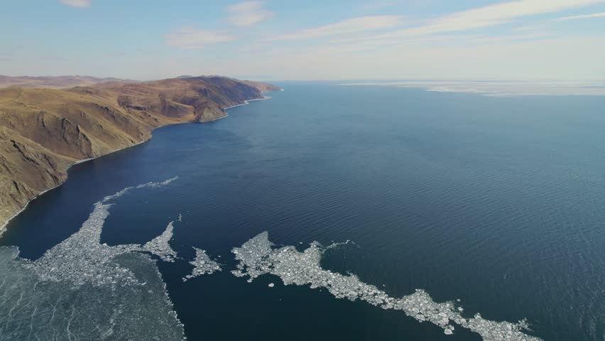 Aerial view of the blue expanse of Lake Baikal with ice floes. Ice drift. Beautiful mountain landscape from the air.