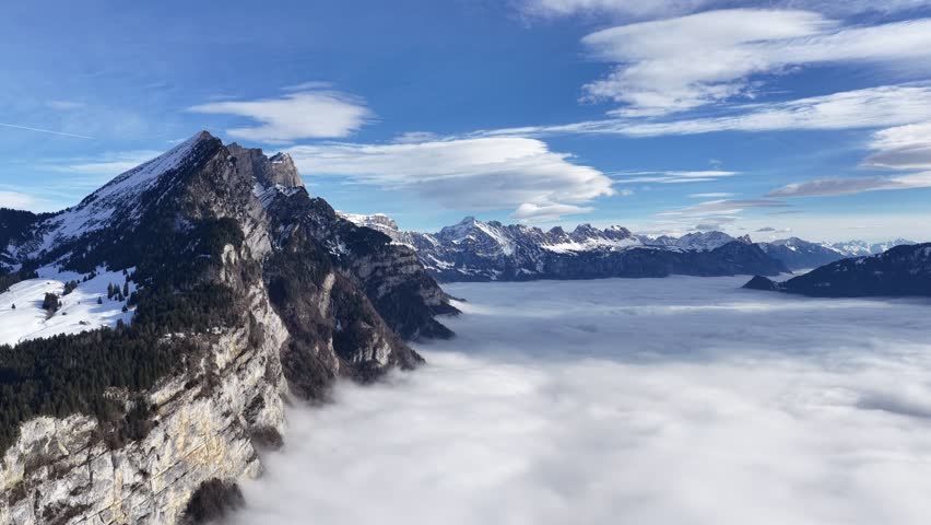 Snow covered alpine cliff and mountains above cloud layer Switzerland