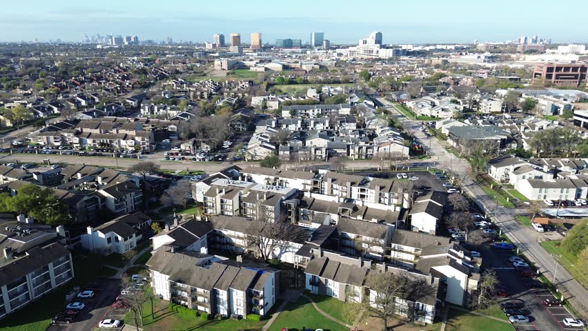 Suburban–urban transition along Fair Oaks Ave near Holly Hill Dr reveals dense multifamily housing leading toward rising commercial towers. Brown roofs, parked cars, muted foliage, Dallas, Texas. USA