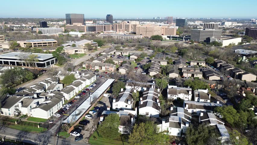 Mixed use residential cluster near Fair Oaks Ave, Pineland Dr apartments arranged around internal drives with offices rising beyond. Light facades, parked vehicles, sparse winter trees, Dallas. USA