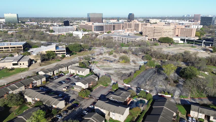 Mixed use expansion view spanning Fair Oaks Ave toward Greenville Ave shows residential rows bordering cleared lot, rising commercial blocks. Roof tones, sparse foliage visual rhythm in Dallas. USA