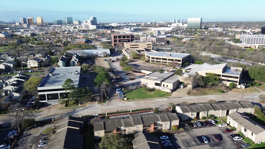 Urban–suburban merge near Fair Oaks Ave and Greenville Ave shows apartments transitioning toward clustered office buildings and distant skyline. Dark roofs, scattered trees in midtown Dallas, TX. USA