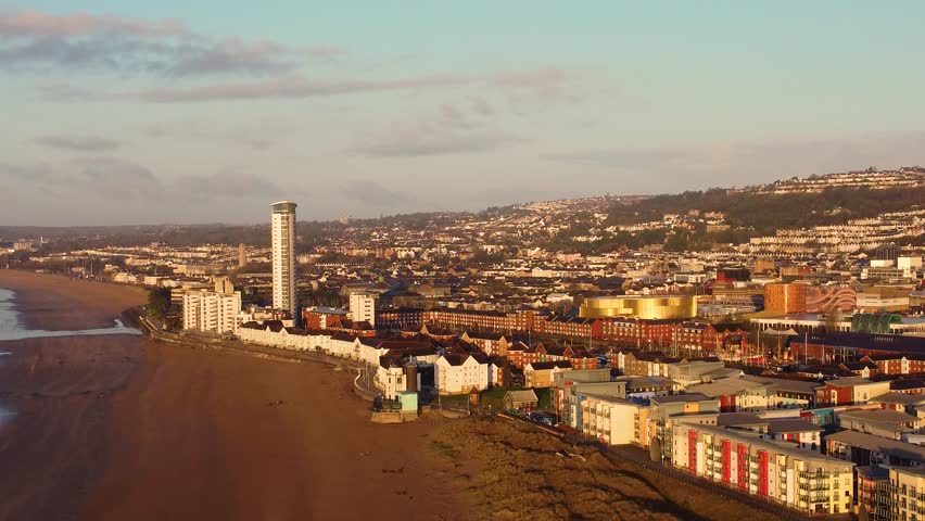 Sideways Aerial of Swansea Cityscape with Tallest Building in Wales with Seaside apartments and City Centre Arena. Landscape of urban environment at sunrise.