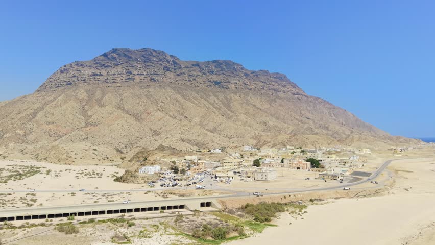 Aerial view of a coastal settlement and desert town located at the base of rugged mountains along the sandy beach of the Gulf of Aden, Car Madow, Somalia.