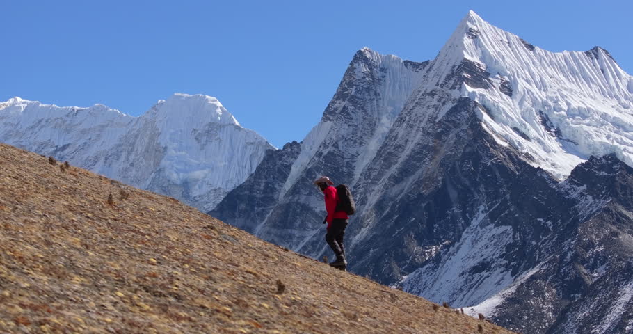 A solo trekker hiking along the Manaslu Circuit Trail in Nepal with dramatic snow-capped Himalayan mountain range rising in the background.