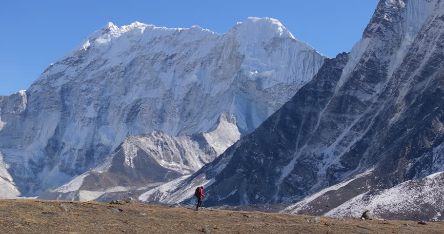 Parallax drone shot of a solo traveler hiking at Kanchenjunga Base Camp in Taplejung, Nepal, with dramatic snow-capped Himalayan mountains rising in the background.