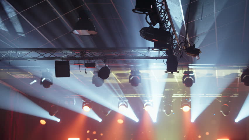 Dynamic stage lighting rig with powerful white and orange beams cutting through atmospheric haze, creating a dramatic effect for concerts, shows, or corporate events