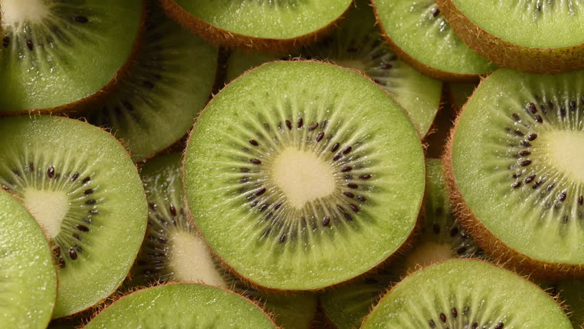 Macro view of fresh kiwi slices with warm summer sunlight moving across the fruit. Juicy green tropical texture creating refreshing natural summer mood and vibrant healthy food background.